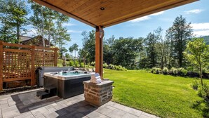 Een terras buiten met een jacuzzi, een barbecue en een stenen openhaard.