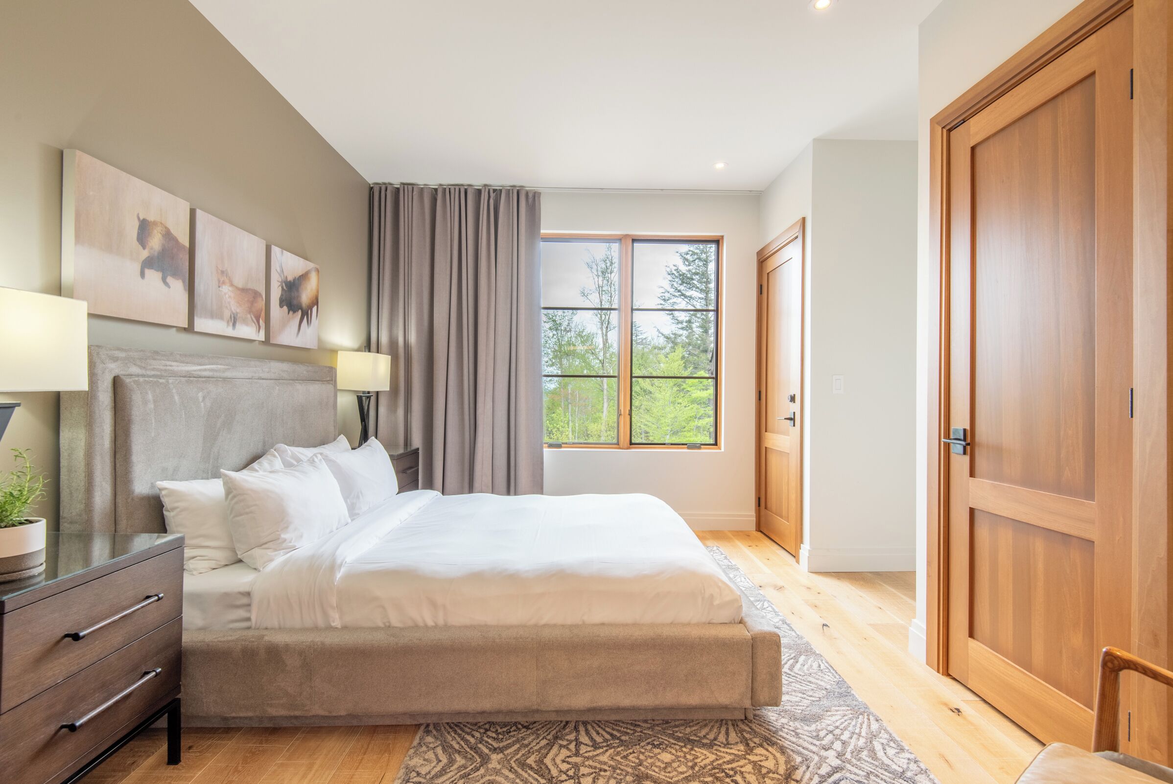 A bedroom with a large bed, a nightstand, a dresser, and a window with curtains.