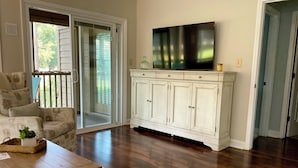 Una sala de estar con piso de madera, un armario blanco, un televisor y un sofá.