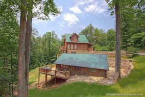 A log cabin with a green roof, a stone foundation, and a wooden deck.