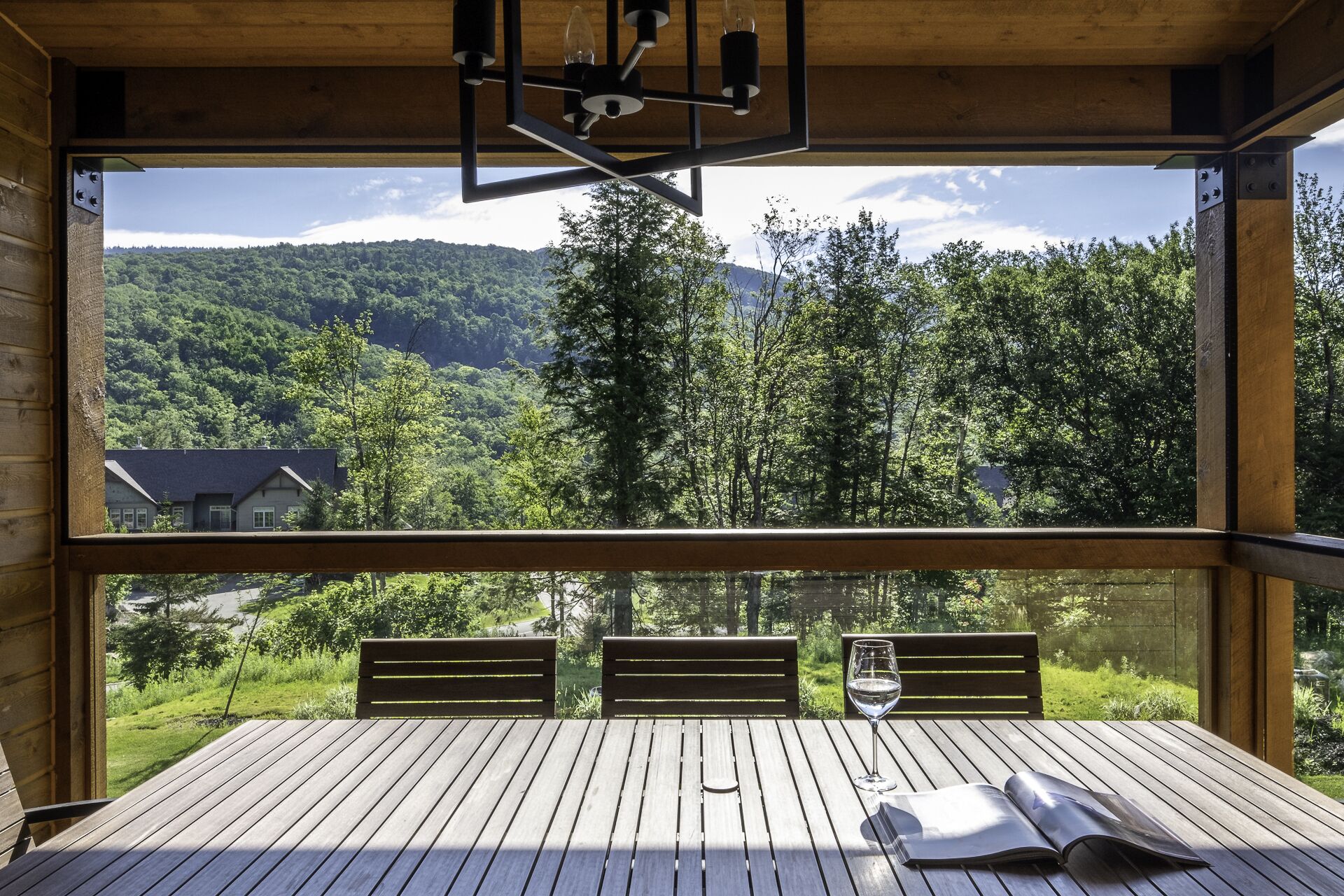 Une terrasse en bois avec une table et des chaises, donnant sur une vallée boisée, avec une montagne qui se profile à l’horizon.