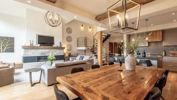 Un vaste espace de vie comprenant une grande table à manger en bois, des sièges confortables, une cheminée et, au fond, une cuisine moderne.