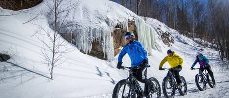 Three people on snow bikes on a snowy slope with a rocky cliff and icicles.