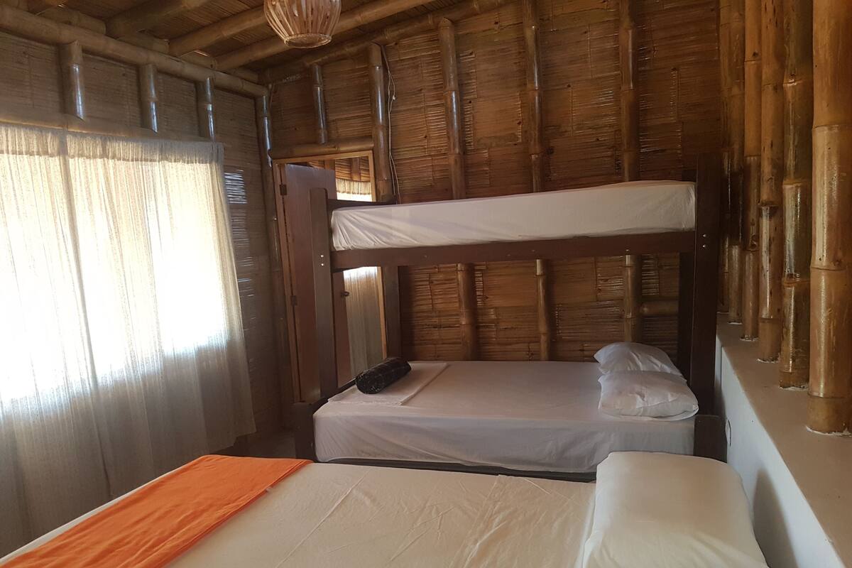 A bunk bed room with a wooden ceiling and walls, a window with curtains, and a bed with white bedding and an orange throw blanket.
