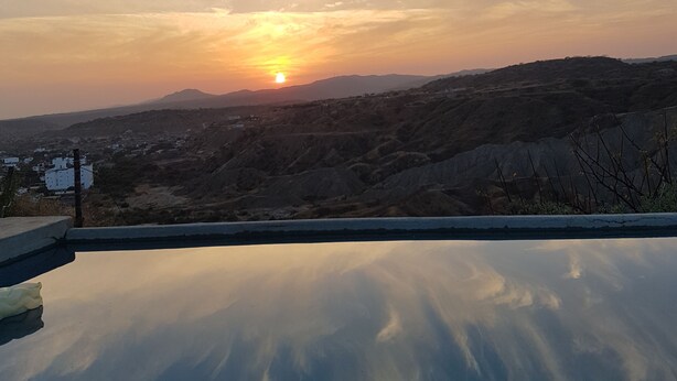 Un ciel dégagé, le soleil se couchant sur un paysage vallonné, son reflet se mire dans une étendue d'eau.