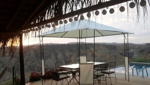Une terrasse extérieure avec une table et des chaises, une piscine et une vue sur des collines rocheuses.