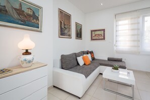 A modern living room with a sofa, a coffee table, and a lamp. There are paintings on the wall and a window with blinds. - Luxury Apartment In Centre Of Split (Split)