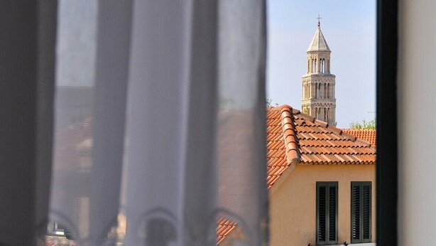 Vista a través de una ventana mostrando un edificio con una torre de campanas y tejas de arcilla.