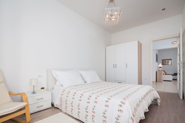 A bedroom with a bed, nightstand, chair, wardrobe, and a chandelier. - Luxury Apartment In Centre Of Split (Split)