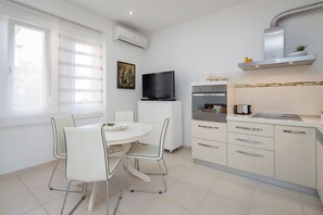 A modern kitchen with white cabinetry, a dining table with chairs, a flat-screen TV, and a built-in oven. - Luxury Apartment In Centre Of Split (Split)