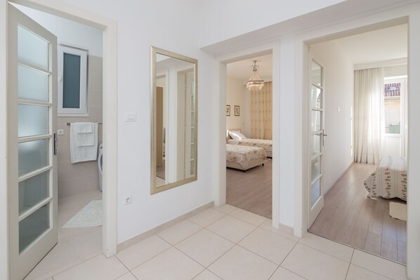 A spacious hallway with a large mirror, a door leading to a bathroom, and a bedroom with a bed and chandelier. - Luxury Apartment In Centre Of Split (Split)