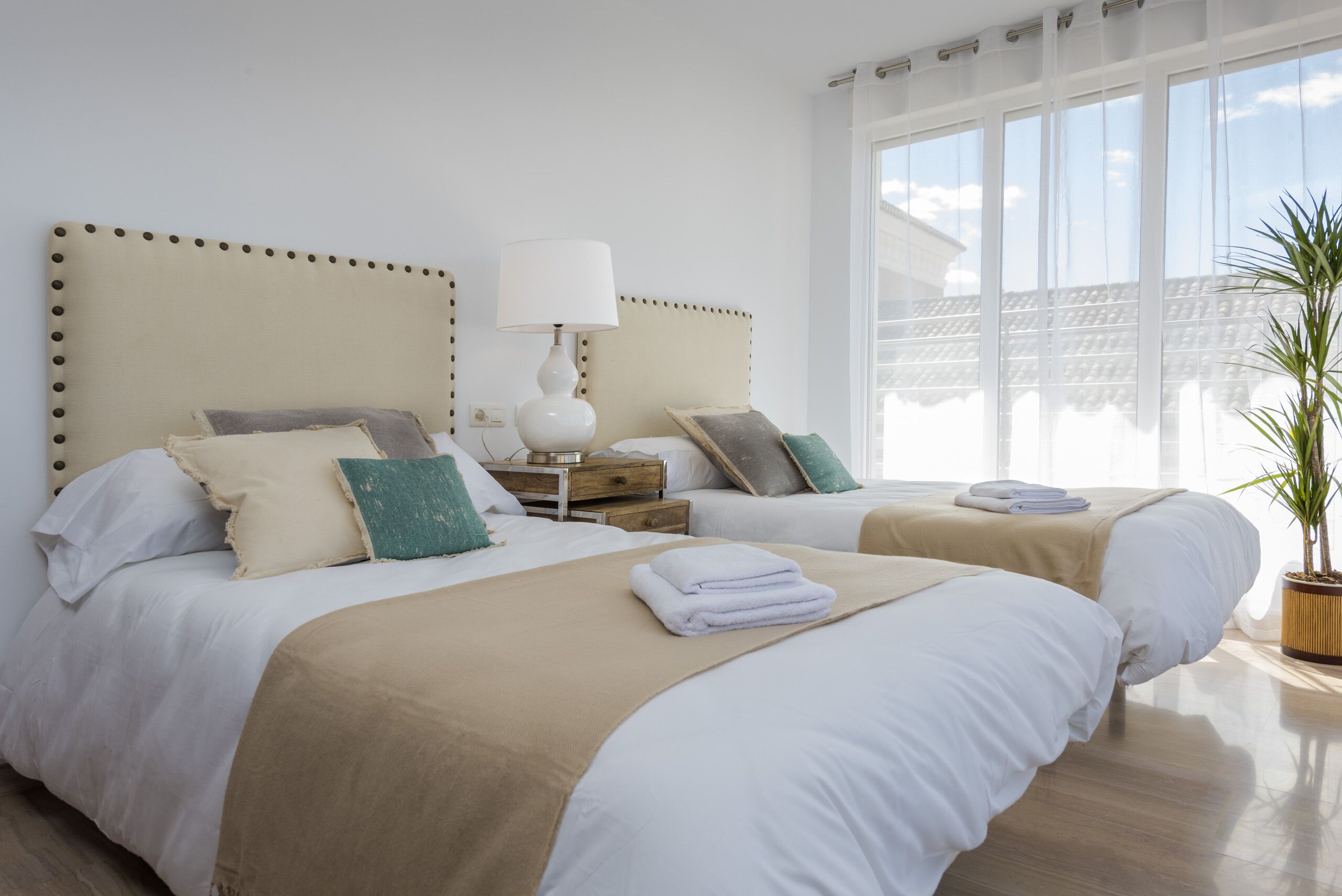 A hotel room with two beds, a nightstand, a lamp, and a large window.