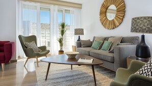 Ein modernes Wohnzimmer mit Sofa, Sesseln, Couchtisch und einem großen Fenster mit durchsichtigen Vorhängen.