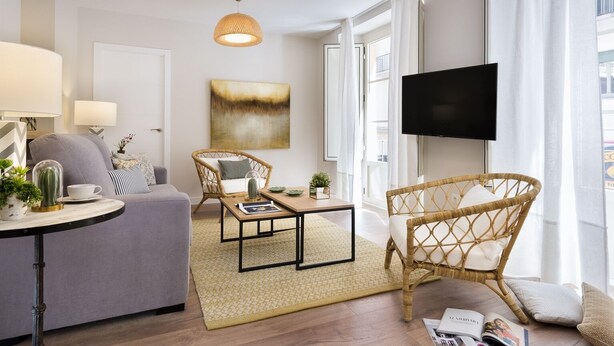 Una sala de estar moderna con un sofá, dos sillones de mimbre, una mesa de centro y un televisor de pantalla plana.