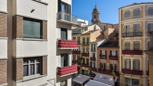 Un edificio de varios pisos con balcones, una torre de iglesia y un café con terraza.