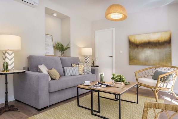 A living room with a grey sofa, a coffee table, a wicker chair, and a painting on the wall.