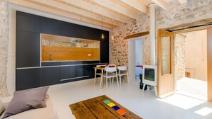 A modern interior with a wooden ceiling, stone walls, a kitchen with dark cabinets, a dining area with white chairs, and a TV in a wooden cabinet. - CASA VELLA (VALL PETIT) - Chalet with terrace in Mancor De La Vall. Free WiFi (Mancor de la Vall)
