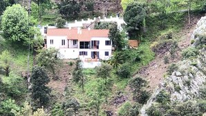 A white building with a red roof surrounded by trees on a hillside.