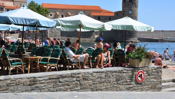 Outdoor seating with umbrellas, a stone wall, and a tower in the background.