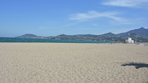 A wide sandy beach with a white lifeguard tower and mountains in the background.