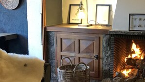 A cozy fireplace with a lit fire, a wicker basket, and framed pictures on a mantel.