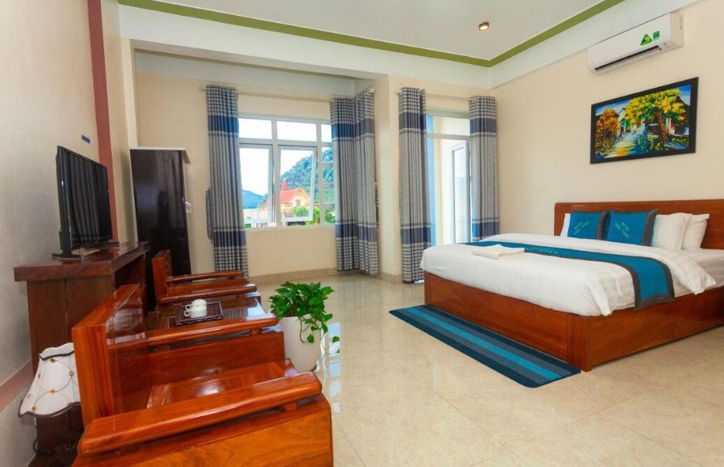 A hotel room with a wooden bed, a desk with a chair, a television, and a window with curtains.