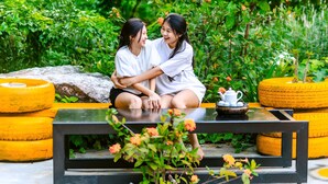 Two people sitting on a bench surrounded by greenery and yellow tires. - Song Toan Hotel (Phong Nha)