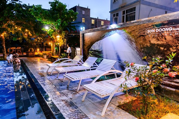 A pool area with lounge chairs, a waterfall feature, and a sign reading "SON DOONG Cave Vietnam." - Song Toan Hotel (Bo Trach)