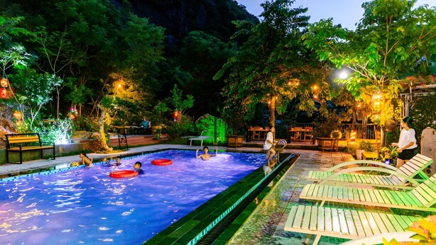 An outdoor swimming pool with lounge chairs and tables, surrounded by trees and ambient lighting. - Song Toan Hotel (Phong Nha)