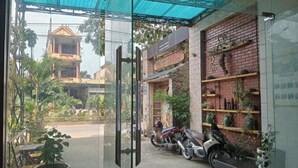 A view through a glass door of a building with a brick facade, a blue awning, and several potted plants. - Song Toan Hotel (Phong Nha)