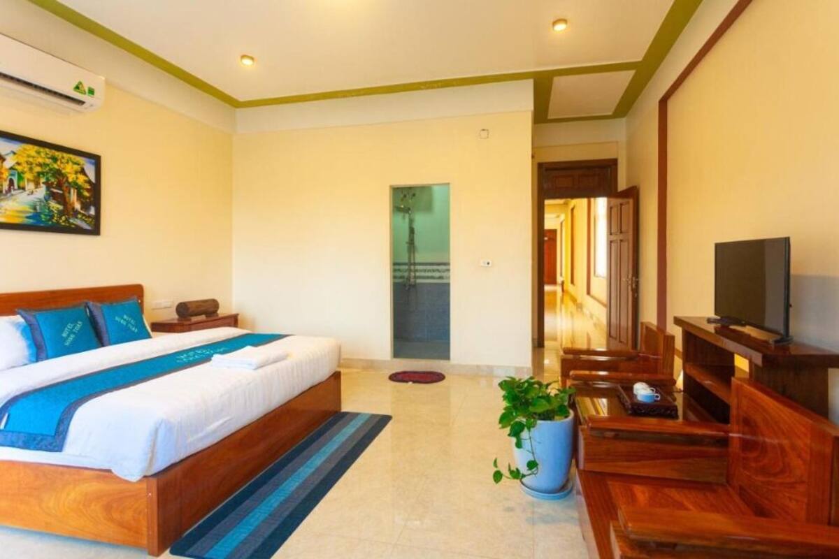 A hotel room with a bed, TV, seating area, and a potted plant.
