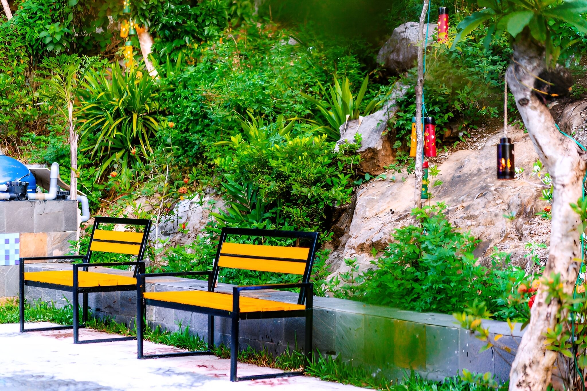 Two black and yellow benches in a park with greenery and a water feature.