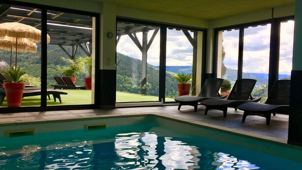 Une piscine intérieure donnant sur un paysage verdoyant grâce à de grandes fenêtres.