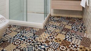 Ein modernes Badezimmer mit einer in Glas abgeschirmten Dusche, einem weißen Fliesenboden und einem Holzbadezimmer-Möbel mit Spiegel darüber.