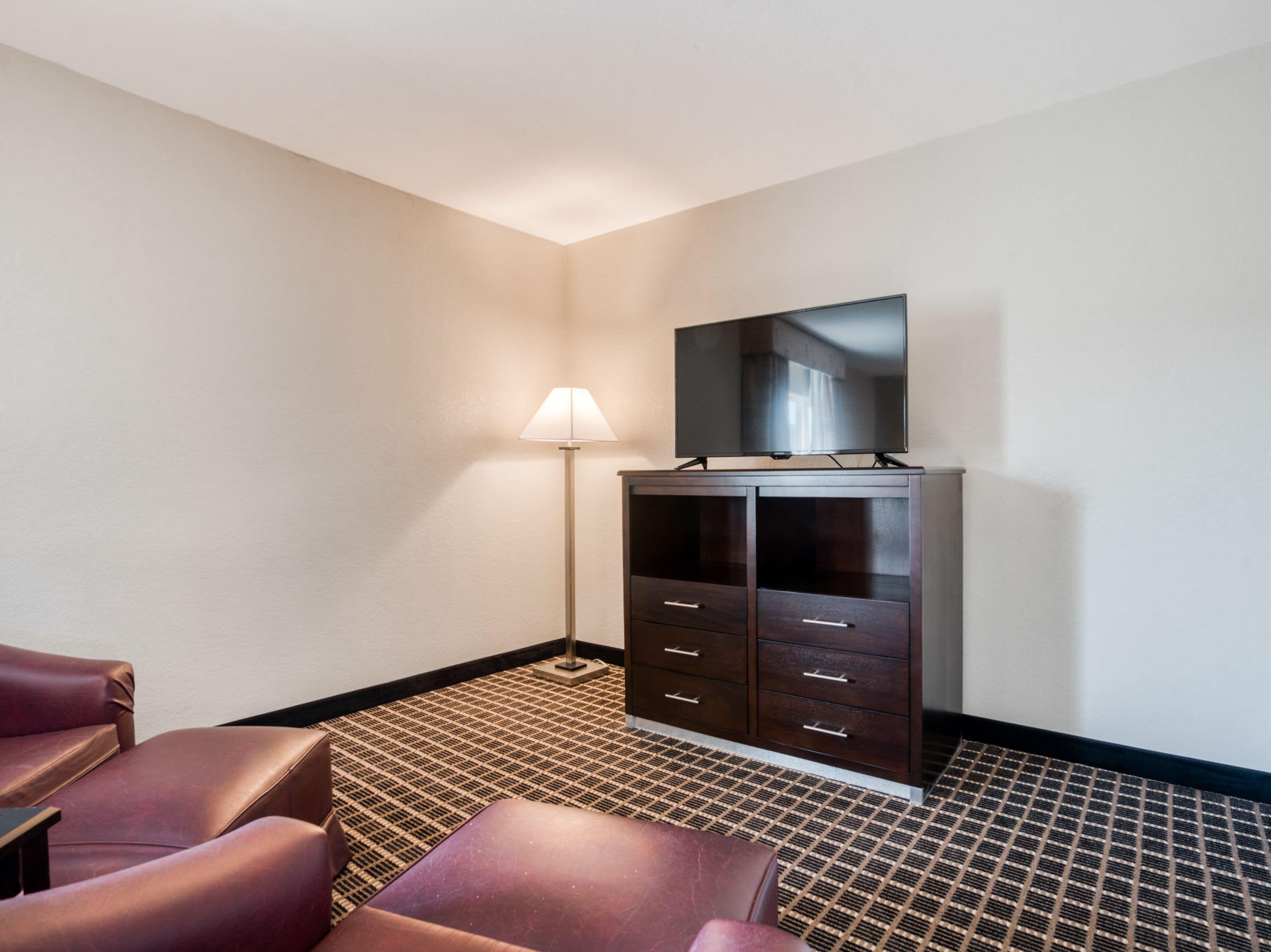 Ein Hotelzimmer mit einem dunklen Holzschrank, einem Flachbildfernseher darauf, einer Stehlampe und zwei Ledersesseln.