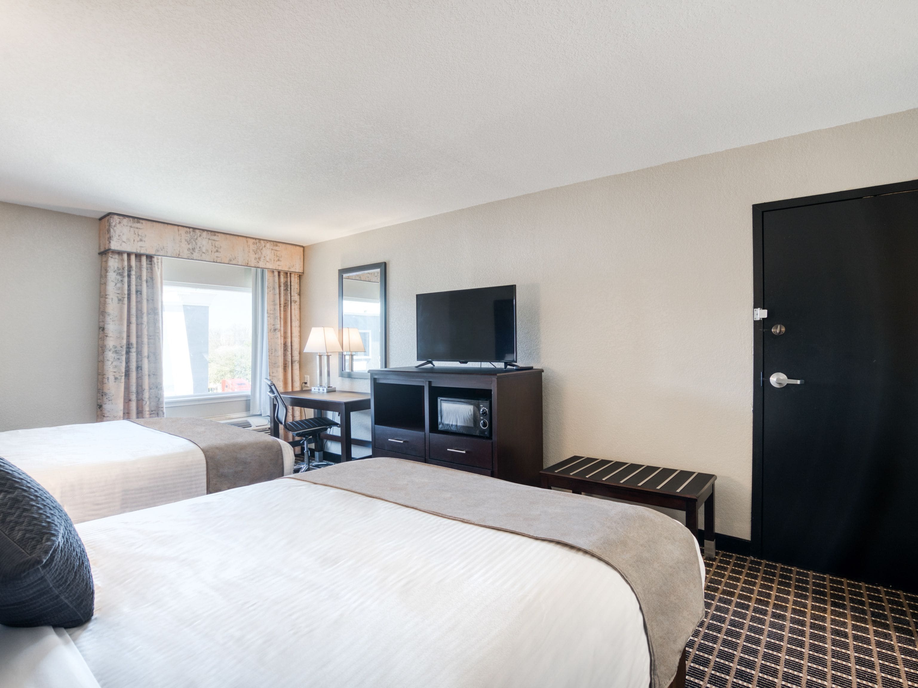 A hotel room with two beds, a desk, a TV, and a door.