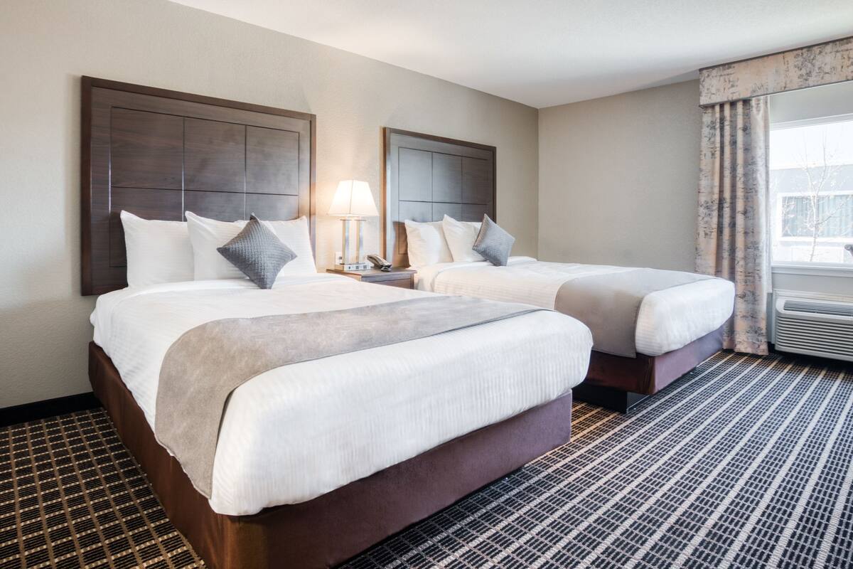 Een hotelkamer met twee bedden, een nachtkastje met een lamp en een raam met gordijnen.