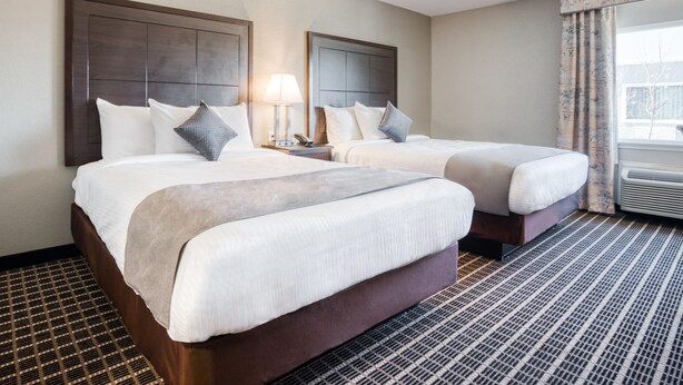 Une chambre d’hôtel avec deux lits, une table de chevet avec une lampe et une fenêtre avec des rideaux.