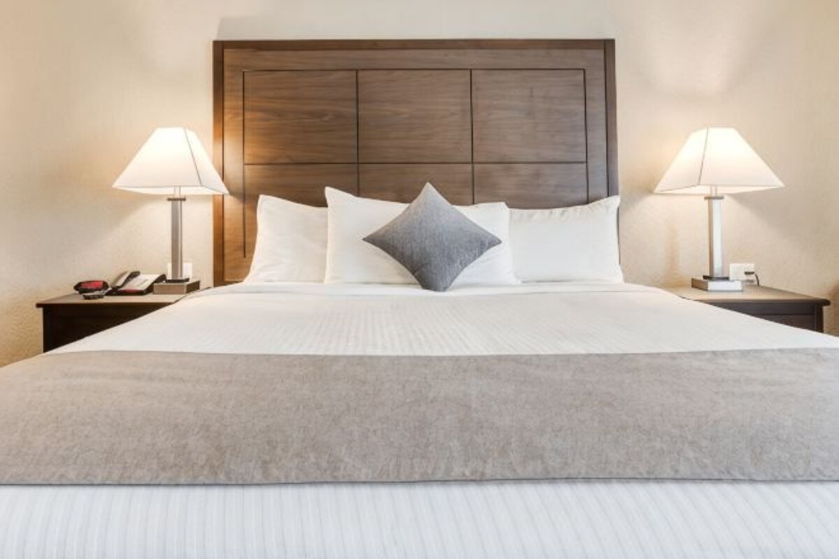 Een opgemaakt bed met een houten hoofdeinde, twee bedlampen en een telefoon op een nachtkastje.