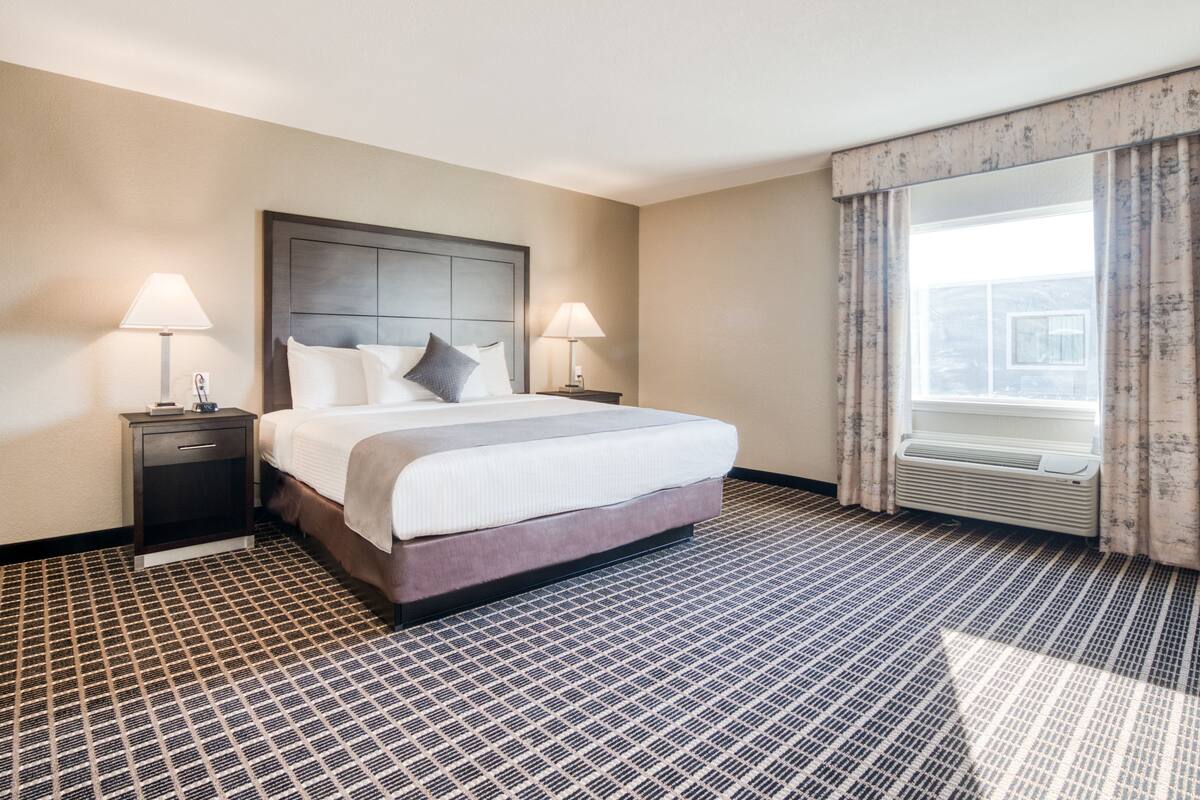 Een hotelkamer met een groot bed, twee nachtkastjes met lampen, een raam met gordijnen en een kamer met een patroon vloer.