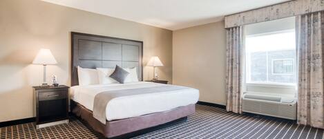 A hotel room with a large bed, two bedside tables with lamps, a window with curtains, and a patterned floor.