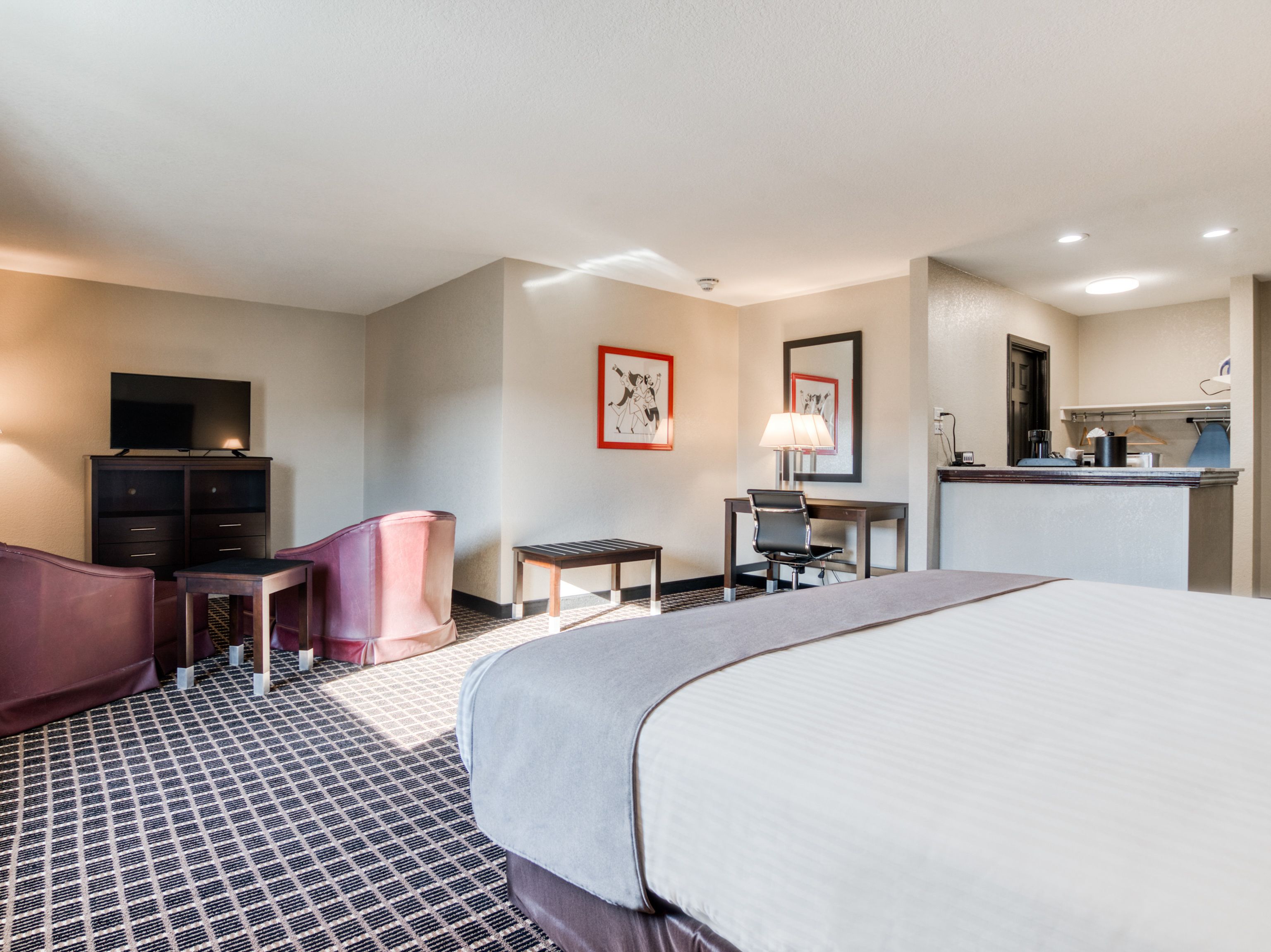 A hotel room with a large bed, a desk, a chair, a television, and a small table.
