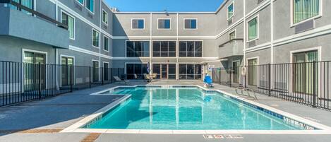 Un bâtiment moderne doté d’une piscine centrale, de nombreux balcons et offrant une vue sur un ciel dégagé.