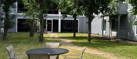 Un patio al aire libre con una mesa redonda y sillas, rodeado de árboles y un edificio moderno al fondo.