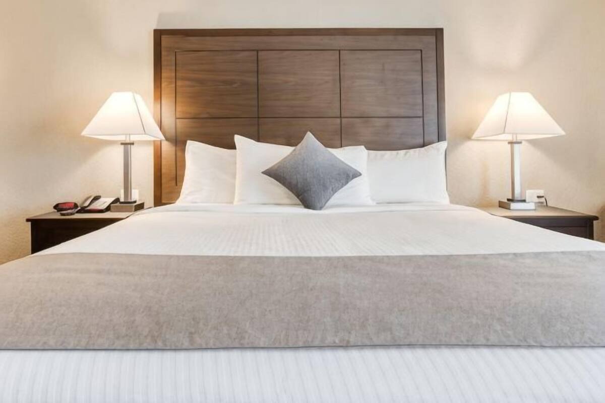 Een opgemaakt bed met een houten hoofdeinde, twee bedlampen en een telefoon op een nachtkastje.