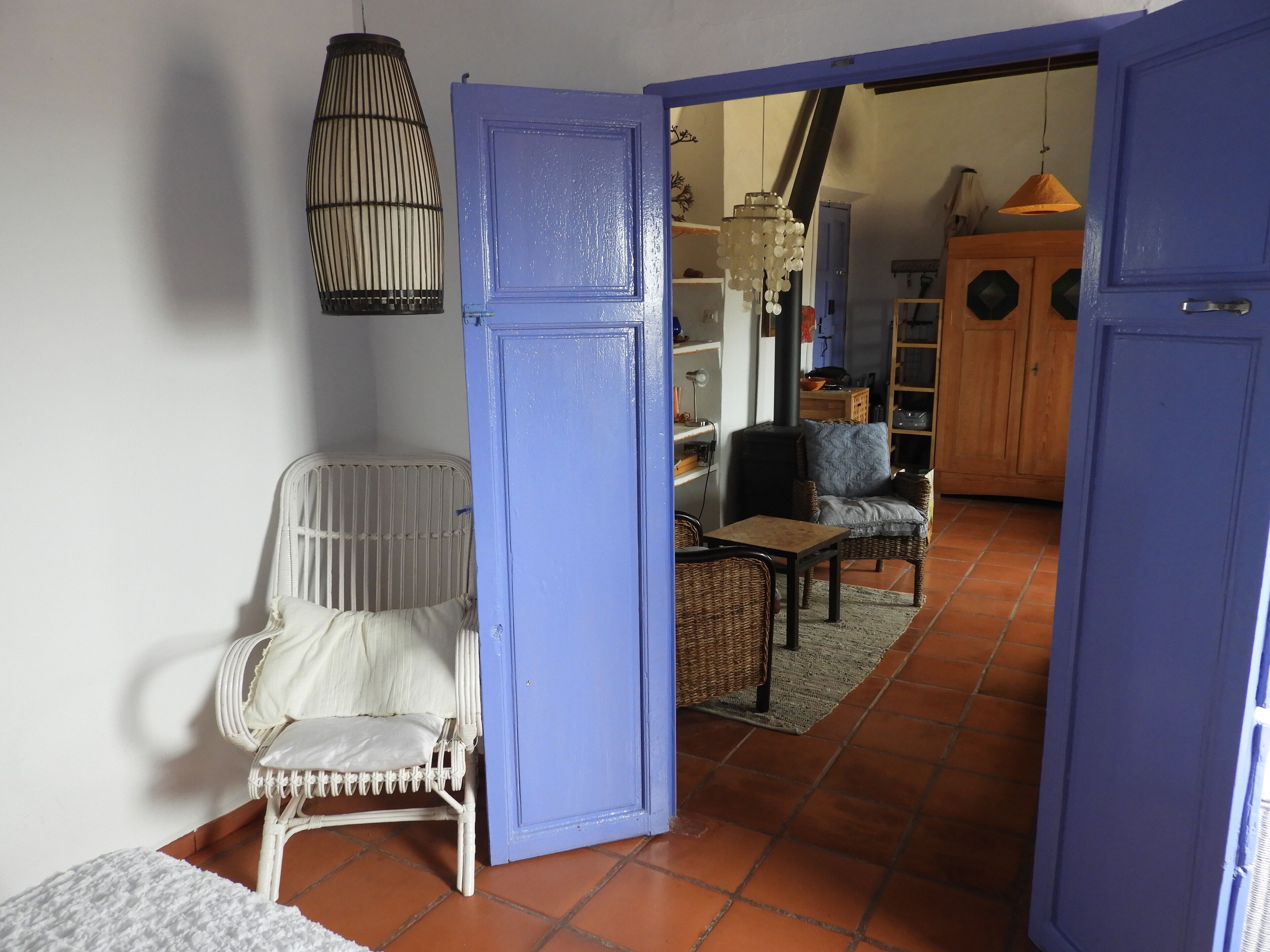 Una habitación con una silla de mimbre blanca, una puerta azul y suelo de baldosas.