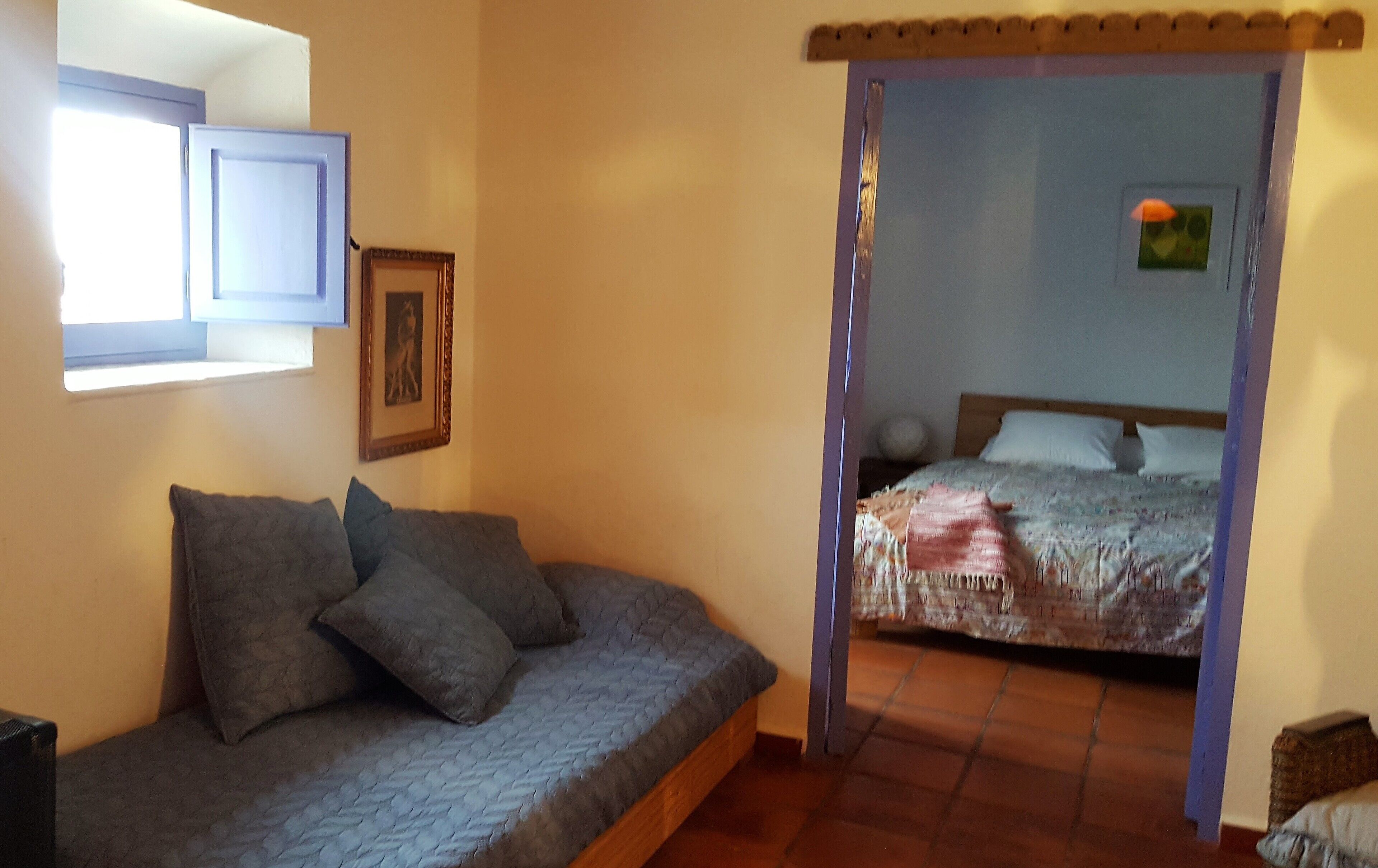 A bedroom with a bed, a sofa, a picture frame, and a window.