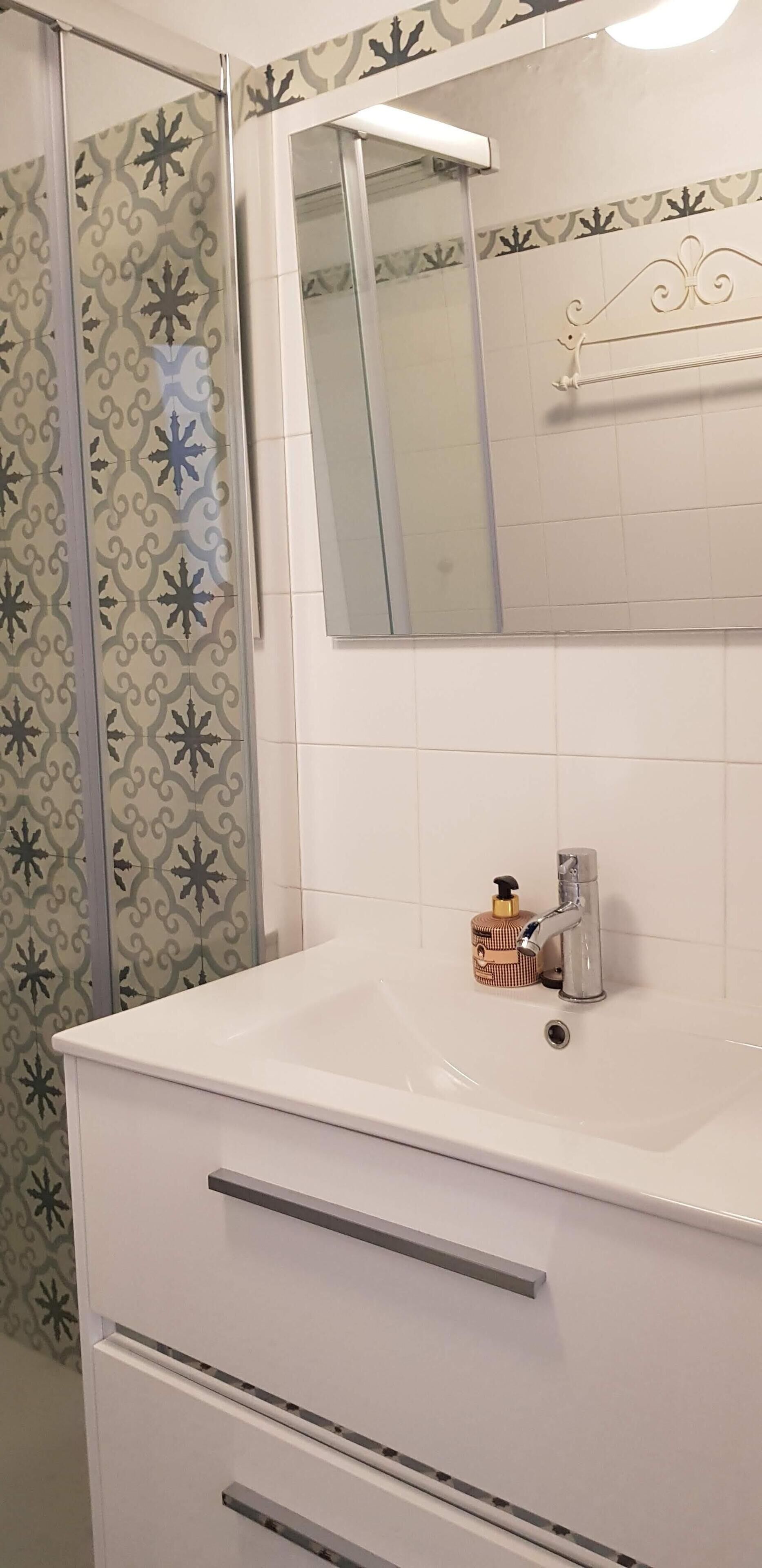 Un baño con lavamanos blanco, espejo y cortina de ducha estampada.