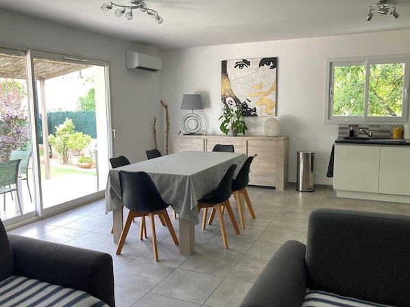 A modern dining area with a table set for four, surrounded by chairs. There is a kitchen area with a sink and cabinets, and a window providing natural light.
