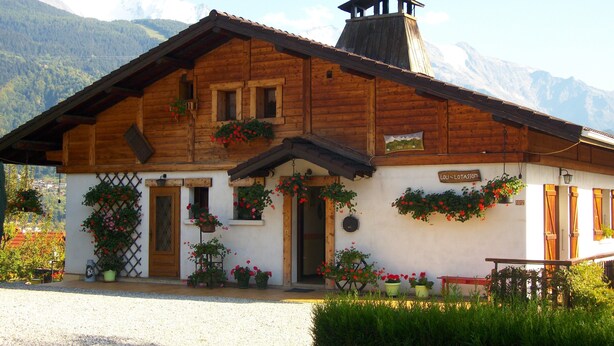 A wooden chalet with a sloped roof, multiple windows, and a sign reading "LOU - LOITASSON".